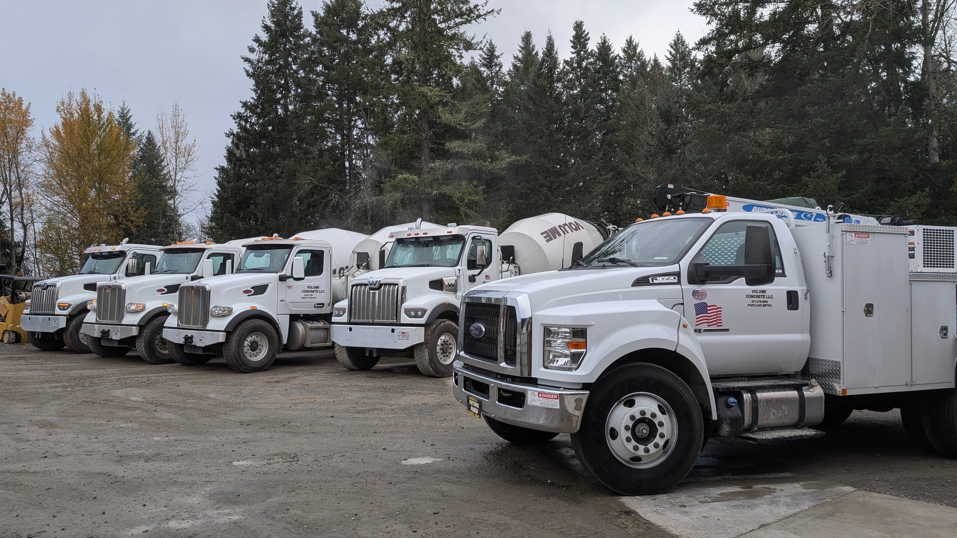 Volume Concrete white barrel trucks and service truck on a gravel lot, VOLUME on the drums, PORTLAND METRO on the door